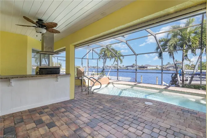 View of pool featuring glass enclosure, ceiling fan, exterior kitchen, exterior bar, and a water view