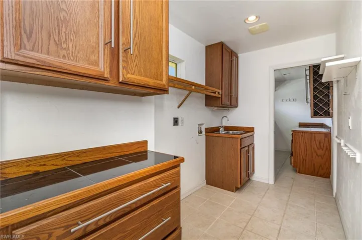 Laundry built in cabinets and tile countertops, light tile patterned floors, and sink