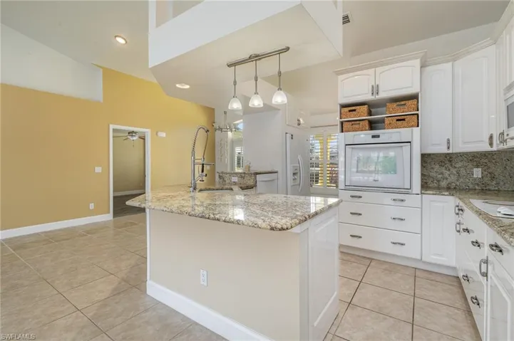 Kitchen with white appliances and granite tops, ceiling fan, white cabinets, a center island, and lofted ceiling