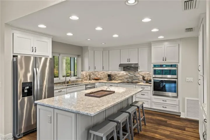 Kitchen with appliances with stainless steel finishes, recessed lighting, light stone countertops, dark wood-type flooring, and white cabinets