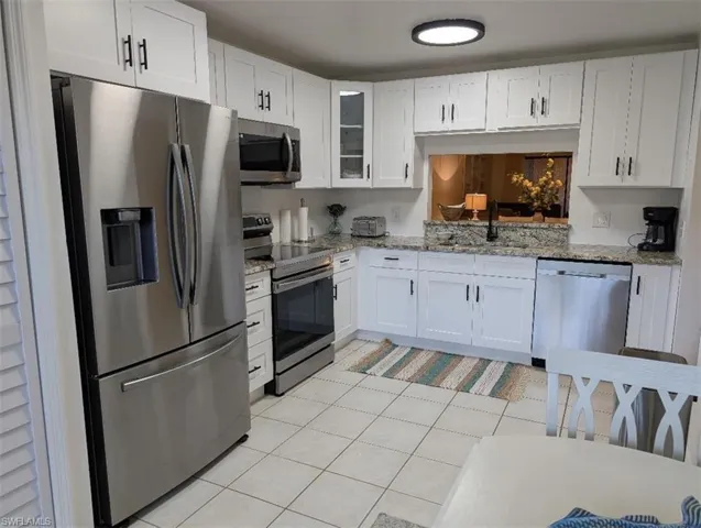 Kitchen with appliances with stainless steel finishes, white cabinets, glass insert cabinets, and light stone counters