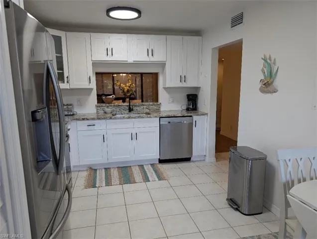 Kitchen with appliances with stainless steel finishes, white cabinetry, light tile patterned flooring, and light stone countertops