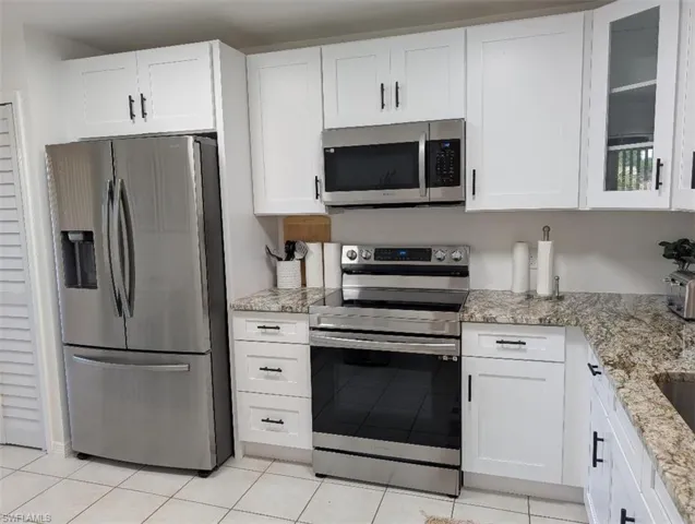 Kitchen with appliances with stainless steel finishes, white cabinets, light stone countertops, and light tile patterned flooring