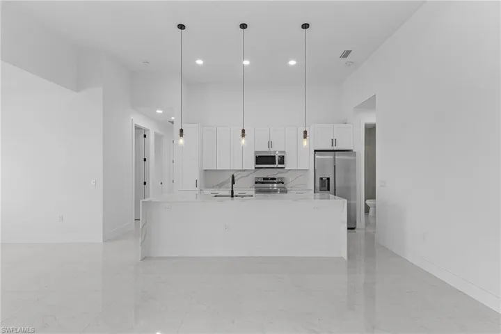 Kitchen featuring marble finish floor, appliances with stainless steel finishes, a towering ceiling, and white cabinetry
