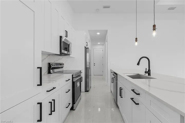 Kitchen with a sink, stainless steel appliances, light stone countertops, and white cabinetry