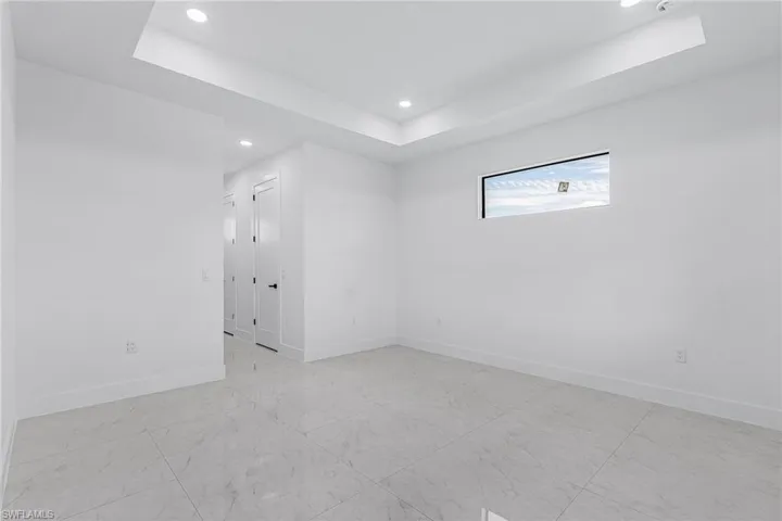 Empty room with a tray ceiling, recessed lighting, baseboards, and marble finish floor