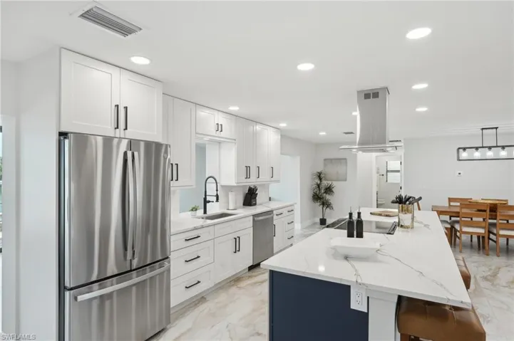 Kitchen with stainless steel appliances, island exhaust hood, light marble finish flooring, white cabinetry, and a sink