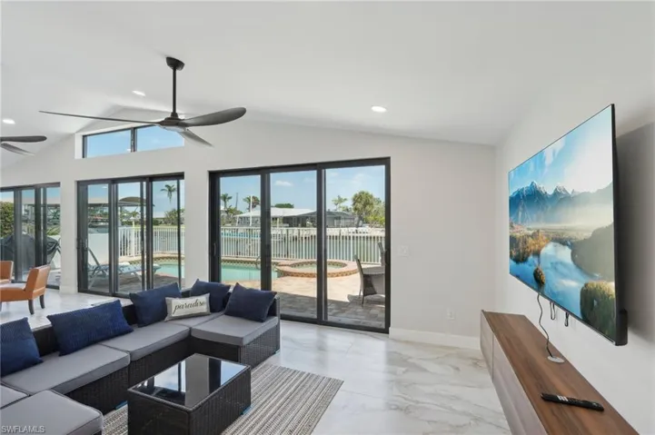 Living room with a ceiling fan, lofted ceiling, light marble finish flooring, recessed lighting, and a water view