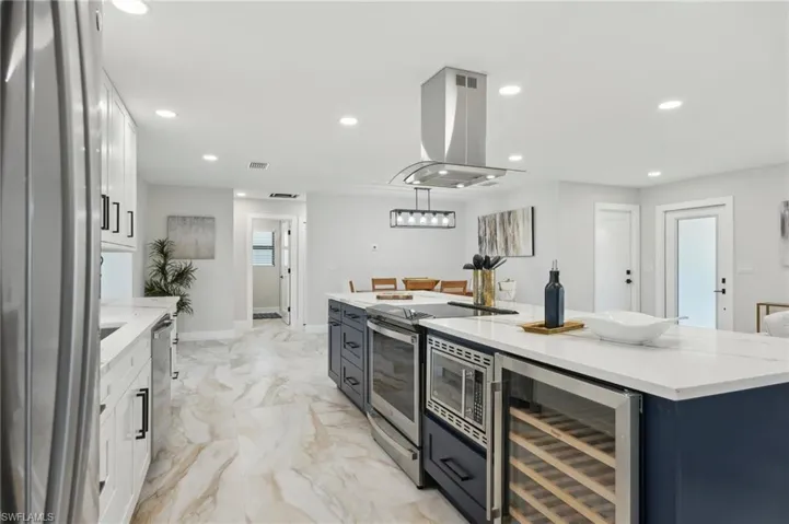Kitchen featuring beverage cooler, appliances with stainless steel finishes, island exhaust hood, white cabinets, and recessed lighting