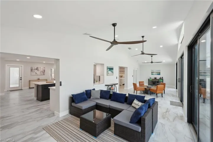Living area featuring a ceiling fan, light marble finish floors, recessed lighting, high vaulted ceiling, and baseboards