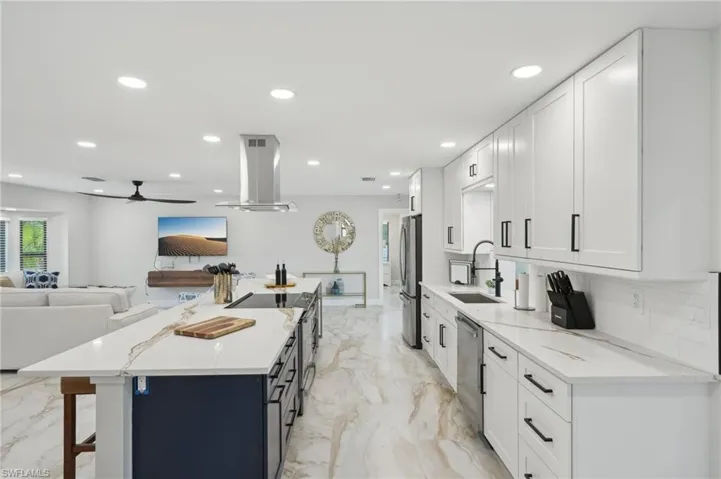 Kitchen featuring a sink, island exhaust hood, stainless steel appliances, light marble finish flooring, and white cabinets