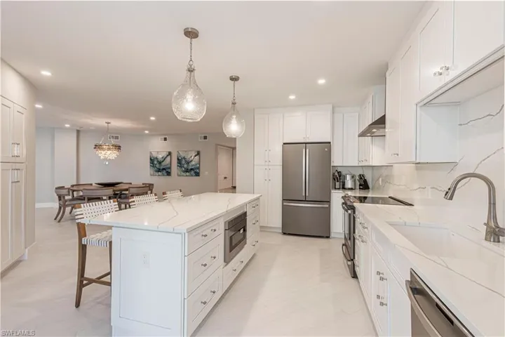 Kitchen featuring white cabinetry, a kitchen island, decorative light fixtures, and appliances with stainless steel finishes