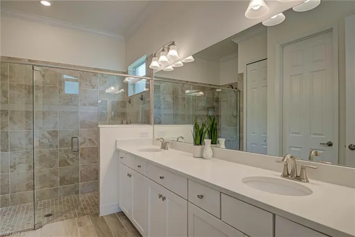 Bathroom with a shower stall, double vanity, ornamental molding, and a closet