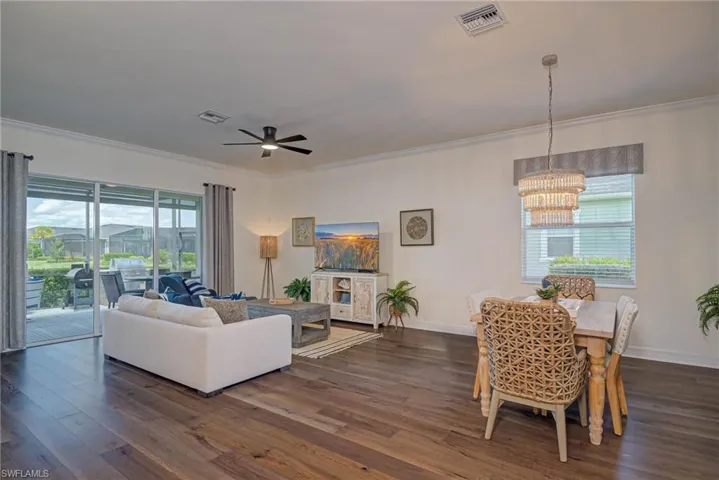 Living room with dark wood-style flooring, crown molding, a ceiling fan, and a chandelier
