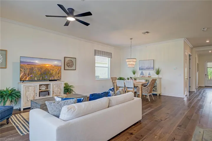 Living room with ornamental molding, dark wood-style flooring, plenty of natural light, and a ceiling fan