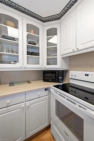 Kitchen featuring white electric range, white cabinets, microwave, light stone countertops, and light wood-style floors