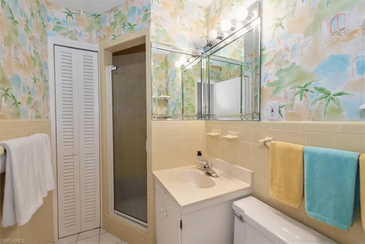 Bathroom featuring tile walls, wallpapered walls, a closet, vanity, and a stall shower