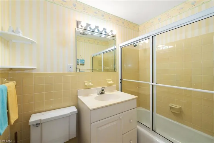 Full bathroom featuring tile walls, enclosed tub / shower combo, vanity, and a wainscoted wall