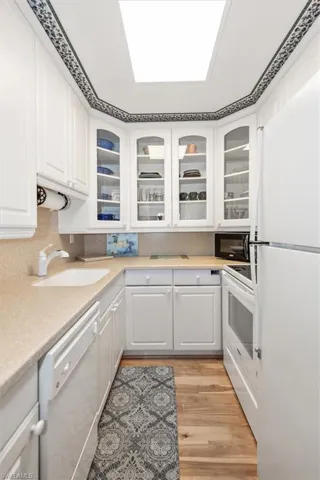 Kitchen with white cabinets, white appliances, glass insert cabinets, and light wood-style flooring