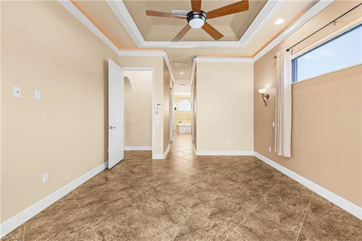Primary bedroom with crown molding, a ceiling fan, plenty of natural light, and a tray ceiling