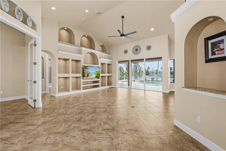 Living room featuring built in shelves, a ceiling fan, high vaulted ceiling, arched walkways, and recessed lighting