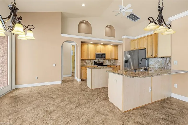 Kitchen with appliances with stainless steel finishes, arched walkways, ceiling fan, stone counters, and backsplash