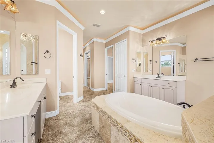 Primary bathroom with ornamental molding, a garden tub, two vanities, and recessed lighting
