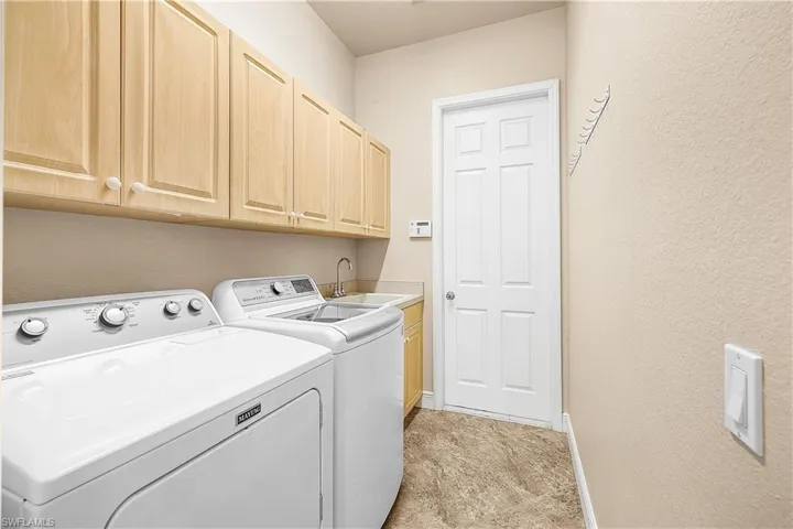 Laundry room featuring washing machine and clothes dryer, laundry sink, and cabinet space