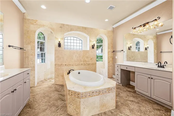 Primary bathroom featuring two vanities, a bath, tile walls, a walk in shower, and recessed lighting