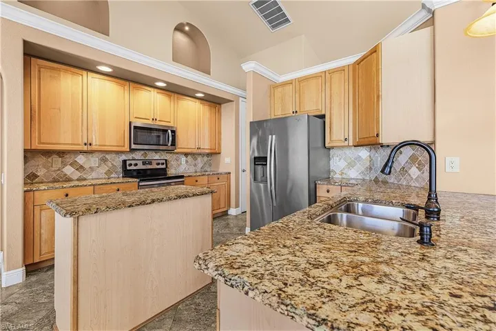 Kitchen with stainless steel appliances, vaulted ceiling, stone counters, backsplash, and a center island