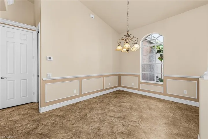 Dining room with vaulted ceiling, a chandelier, wainscoting, and tile flooring
