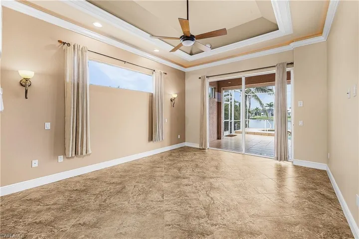 Primary bedroom with ornamental molding, ceiling fan, a tray ceiling, and tile flooring