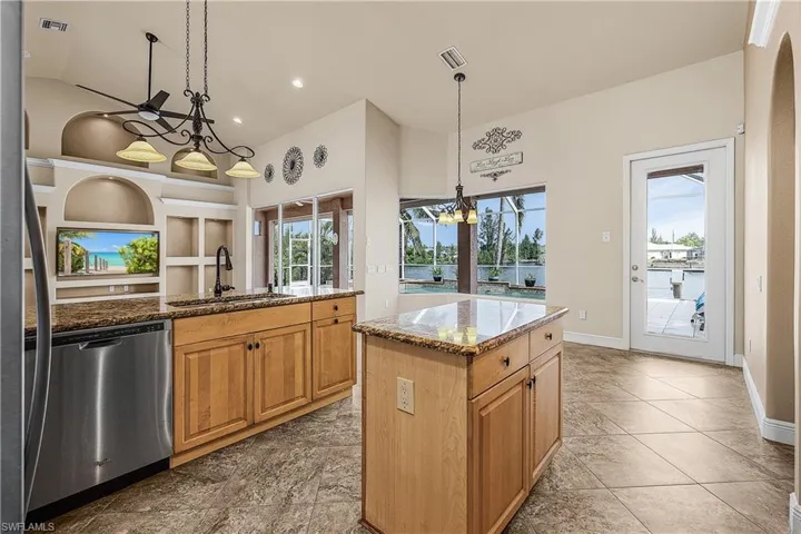 Kitchen with dishwasher, a chandelier, stone countertops, high vaulted ceiling, and decorative light fixtures