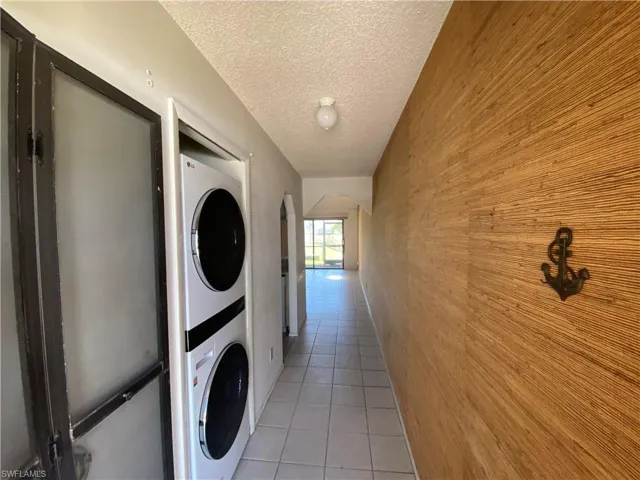 Laundry room with light tile floors, stacked washing maching and dryer, wood walls, and a textured ceiling