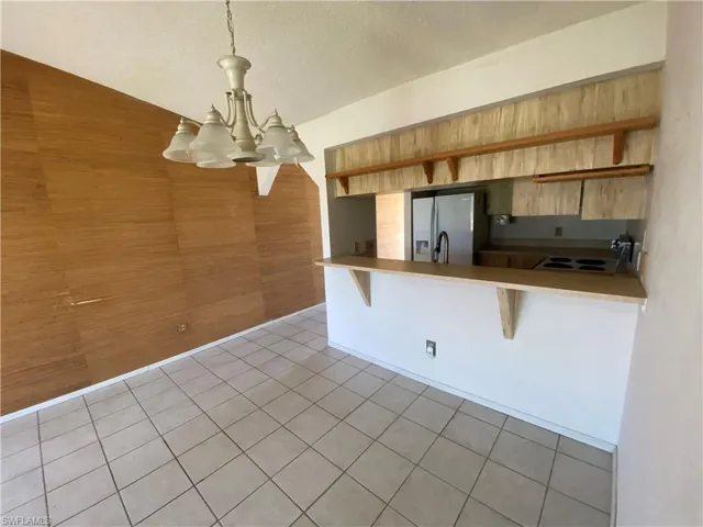 Kitchen featuring stainless steel fridge with ice dispenser, a textured ceiling, decorative light fixtures, a chandelier, and a kitchen bar