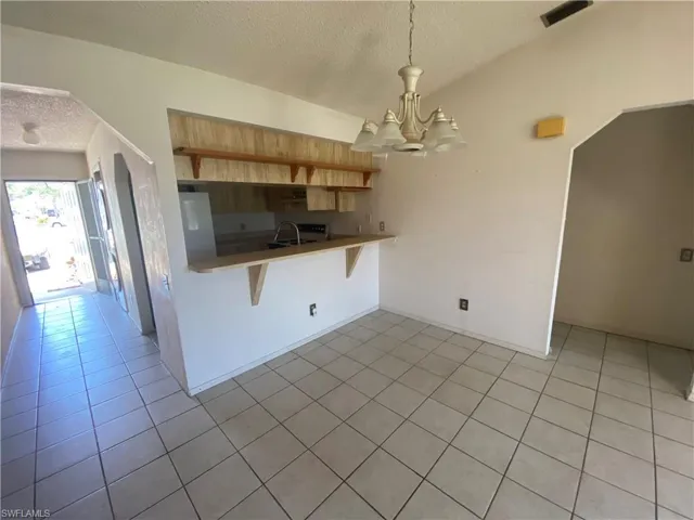 Kitchen featuring a textured ceiling, decorative light fixtures, a notable chandelier, light tile flooring, and a kitchen bar