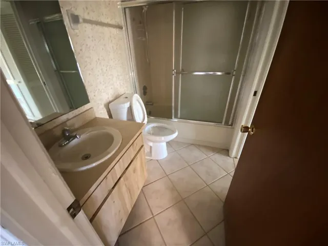 Full bathroom featuring combined bath / shower with glass door, oversized vanity, toilet, and tile floors