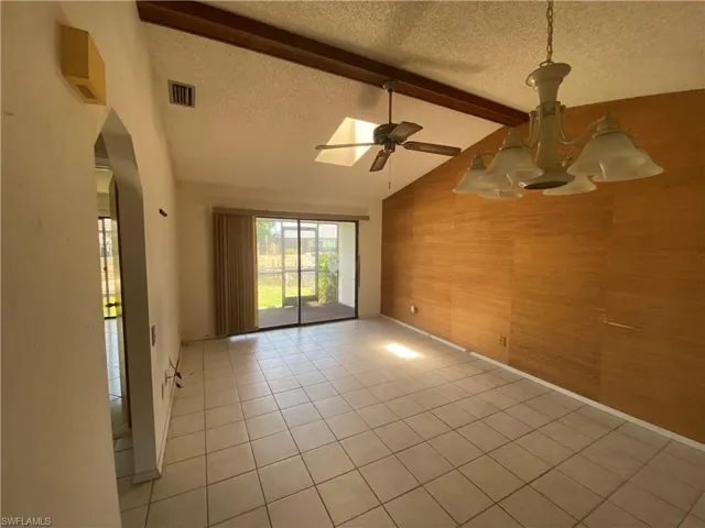 Empty room featuring a textured ceiling, lofted ceiling with beams, ceiling fan, and light tile floors