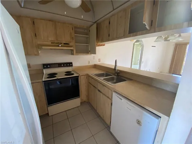 Kitchen with white appliances, sink, light tile flooring, ceiling fan, and light brown cabinetry