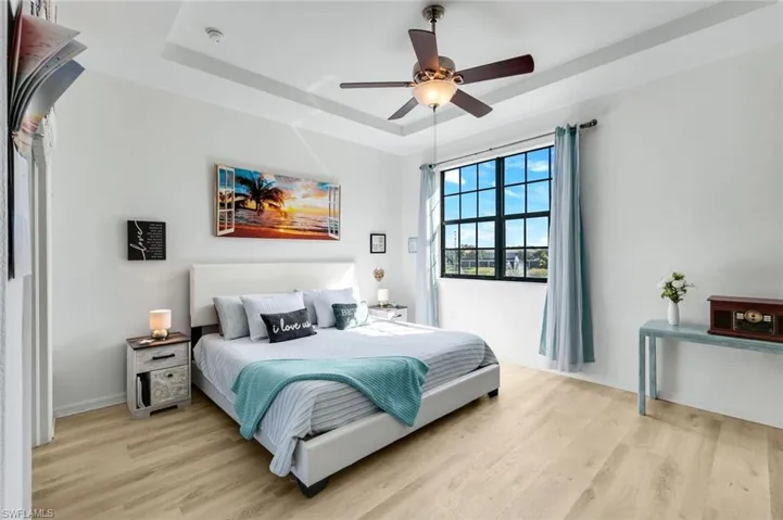 Bedroom with a tray ceiling, light wood-type flooring, and a ceiling fan