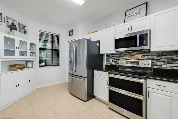 Kitchen with stainless steel appliances, glass insert cabinets, white cabinetry, decorative backsplash, and light tile patterned flooring