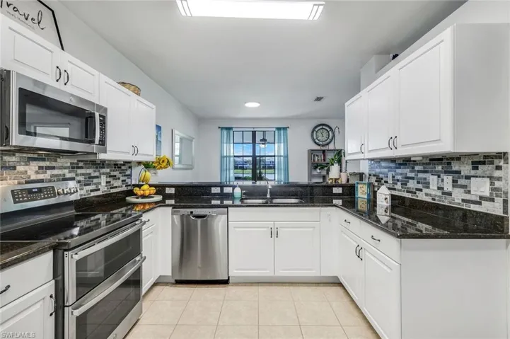 Kitchen with appliances with stainless steel finishes, decorative backsplash, dark stone countertops, light tile patterned floors, and recessed lighting