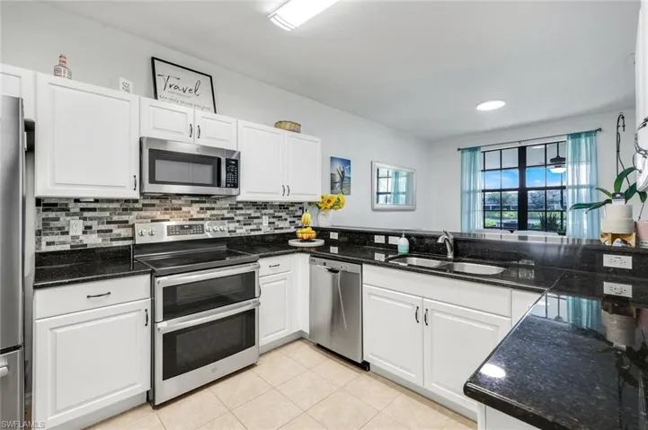 Kitchen with stainless steel appliances, white cabinets, backsplash, light tile patterned floors, and dark stone countertops