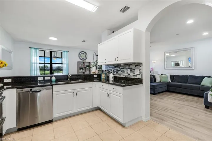 Kitchen with open floor plan, stainless steel dishwasher, light tile patterned floors, white cabinetry, and dark stone countertops