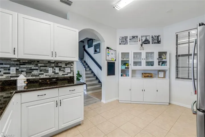 Kitchen with white cabinetry, dark stone counters, freestanding refrigerator, decorative backsplash, and light tile patterned floors