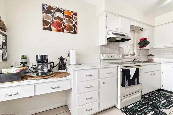 Kitchen with white electric range oven, light countertops, white cabinetry, and decorative backsplash