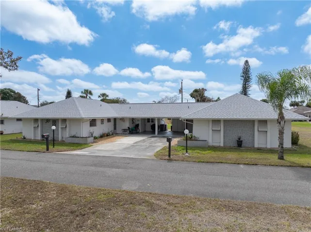 Ranch-style house with a carport, a front yard, a shingled roof, and driveway