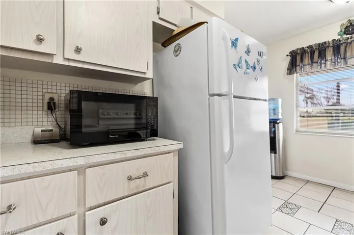 Kitchen with freestanding refrigerator, light countertops, black microwave, light tile patterned floors, and decorative backsplash