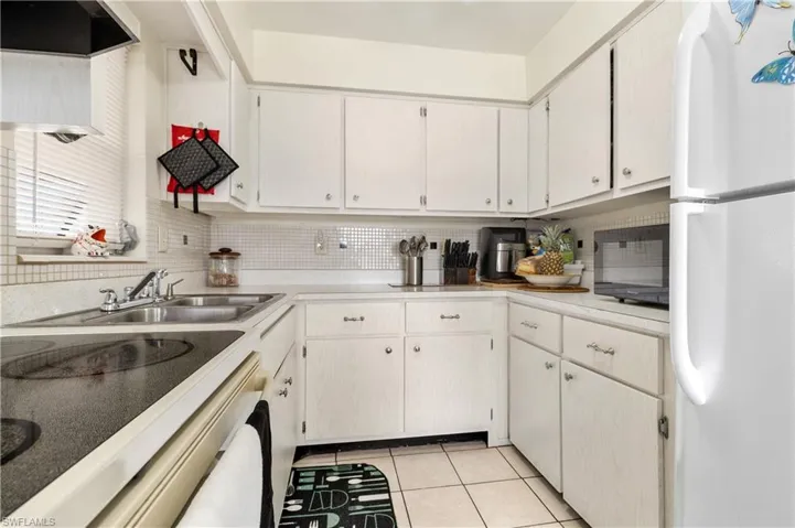 Kitchen with freestanding refrigerator, light countertops, black microwave, light tile patterned flooring, and electric range oven