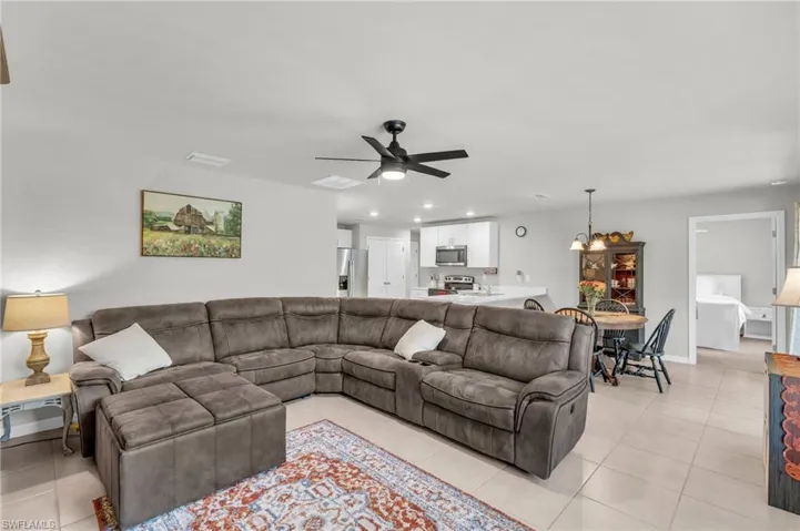 Living room with light tile patterned flooring and ceiling fan with notable chandelier